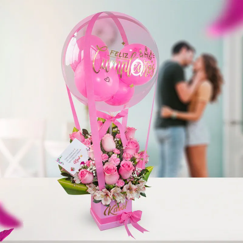 Arreglo floral con rosas color fucsia y un globo de burbuja transparente con mensaje de 'Feliz Cumpleaños', perfecto para celebraciones.