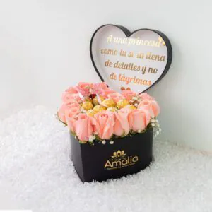 Arreglo floral en caja en forma de corazón con rosas rosadas y detalles dorados, perfecto para cumpleaños y aniversarios.