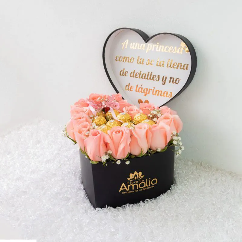 Arreglo floral en caja en forma de corazón con rosas rosadas y detalles dorados, perfecto para cumpleaños y aniversarios.