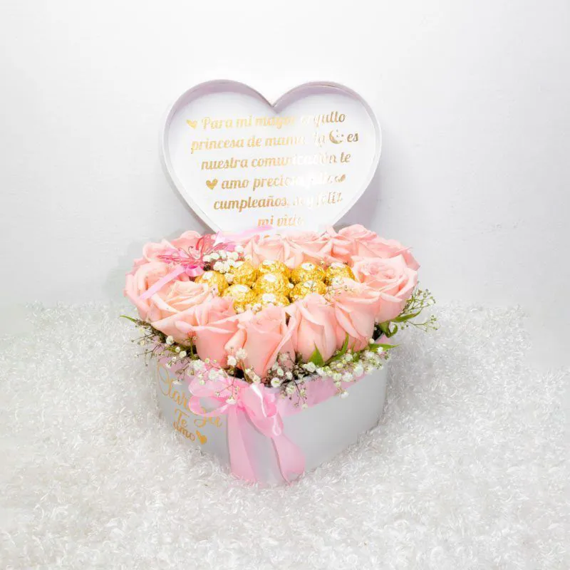 Arreglo floral en caja en forma de corazón con rosas rosadas y detalles dorados, perfecto para cumpleaños y aniversarios.