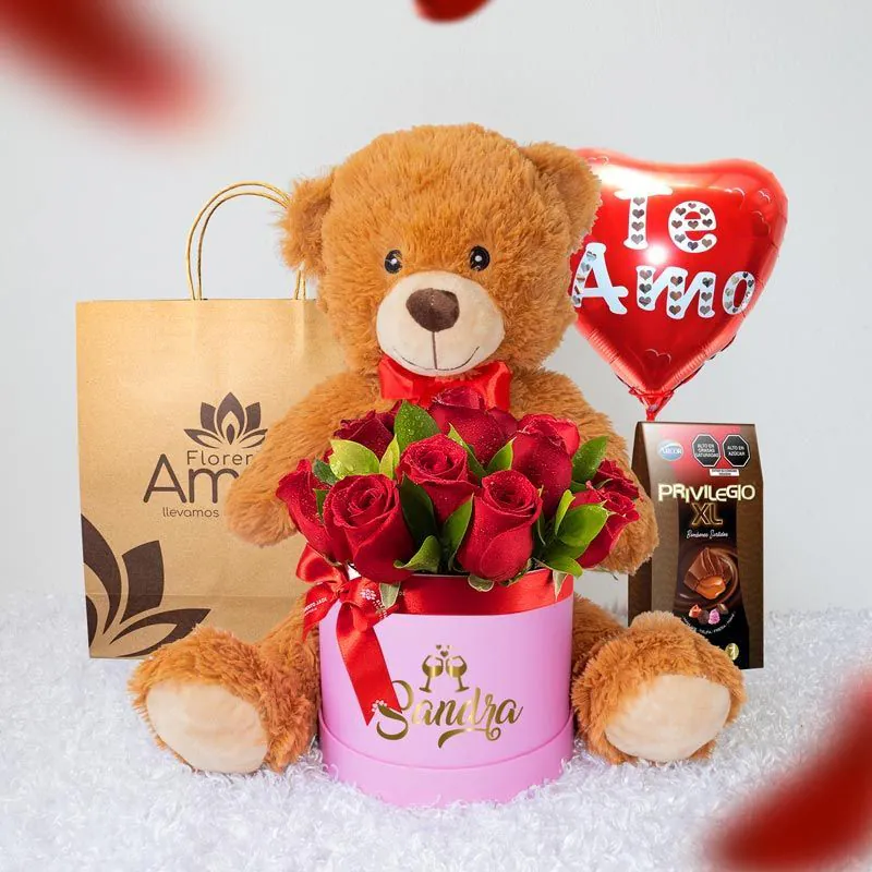 Arreglo de rosas rojas en caja personalizada con el nombre 'Sandra', acompañado de un peluche de oso y chocolates, ideal para un regalo de amor.