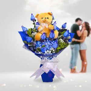 Arreglo de rosas azules con peluche de osito en un ramo elegante.