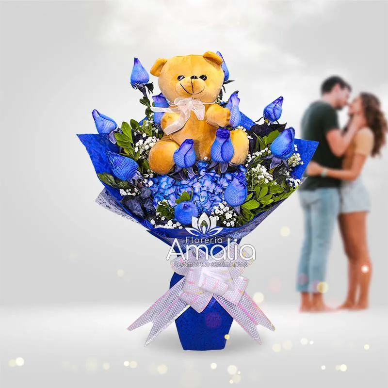 Arreglo de rosas azules con peluche de osito en un ramo elegante.