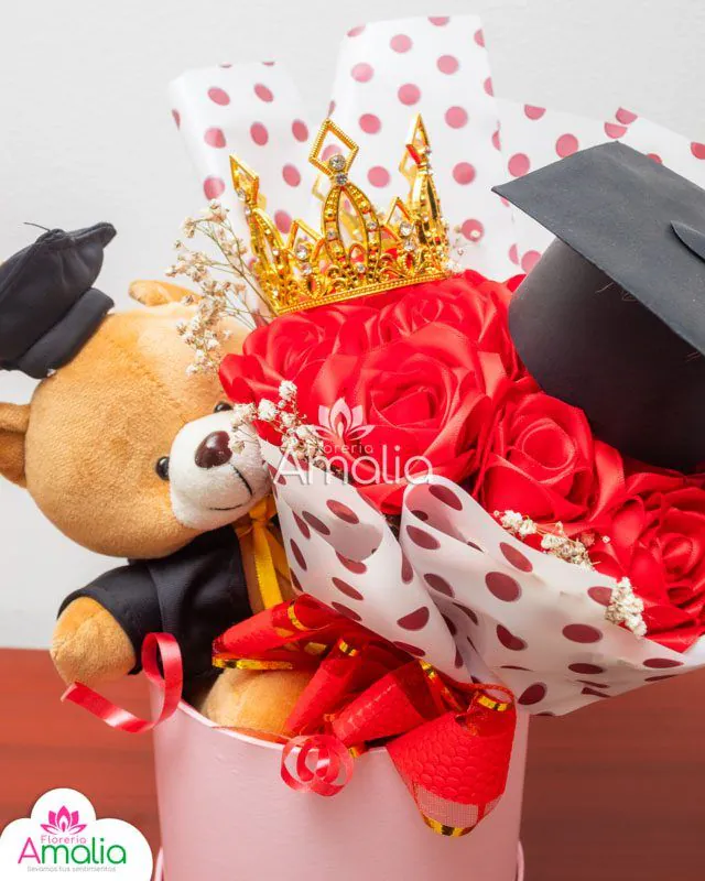 Caja decorativa con peluche de graduación, corona dorada y rosas rojas, ideal para celebrar logros académicos.