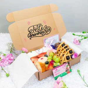 Caja de desayuno para aniversario con mensaje ‘Feliz Aniversario’, incluye frutas frescas, waffles, chocolates decorados, jugo natural, pan artesanal y tarjeta personalizada.