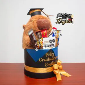 Caja de graduación personalizada con peluche de capibara, dulces variados y mensaje especial, ideal para celebrar logros académicos.
