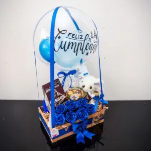Caja de cumpleaños con globo personalizado, rosas azules, peluche blanco y dulces variados.