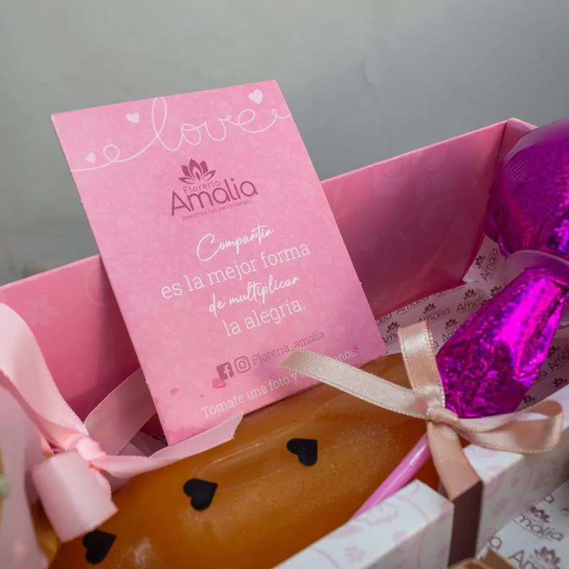 Desayuno sorpresa en caja rosa con mini ramo de flores, croissant relleno, jugo natural y torta decorada con corazones, ideal para regalos especiales.