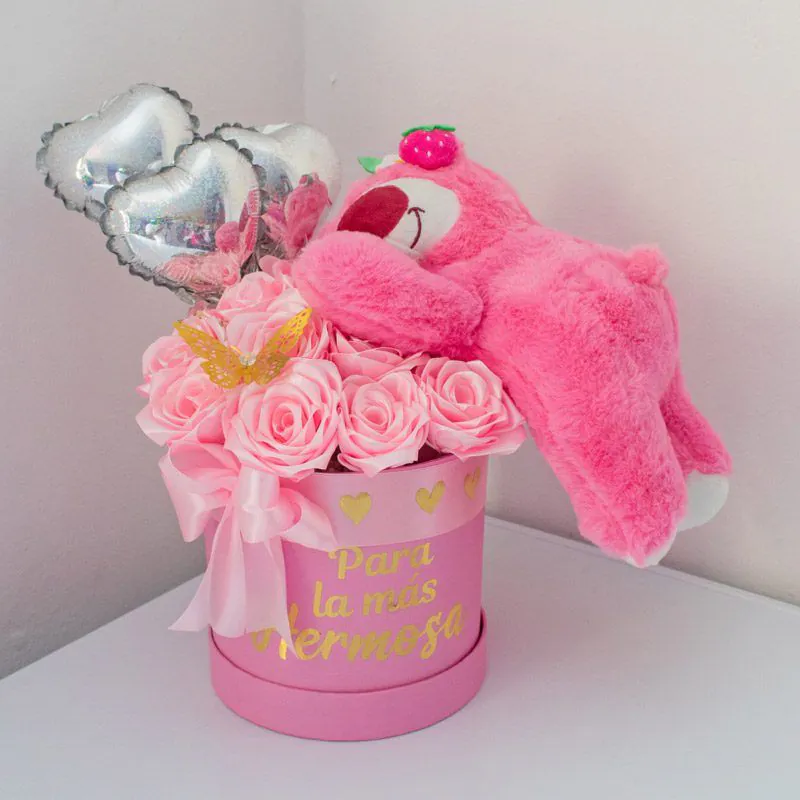 Arreglo floral con peluche rosa tipo Lotso, rosas rosadas, globos metálicos en forma de corazón y caja personalizada con la frase “Para la más hermosa”.
