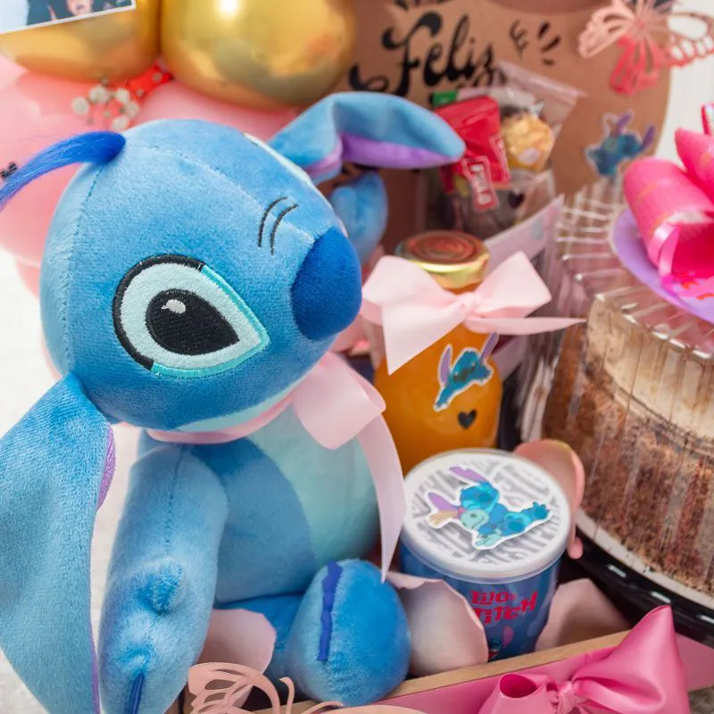 “Cumpleaños sorpresa con peluche Stitch, torta decorada, globo burbuja, arco de globos y fotos personalizadas sobre base, ideal para regalar.”