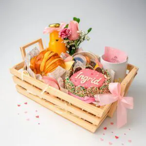 Desayuno sorpresa en fuente de madera con mini torta personalizada, pan brioche, jugo, frutas, taza y mini florero – Florería Amalia.
