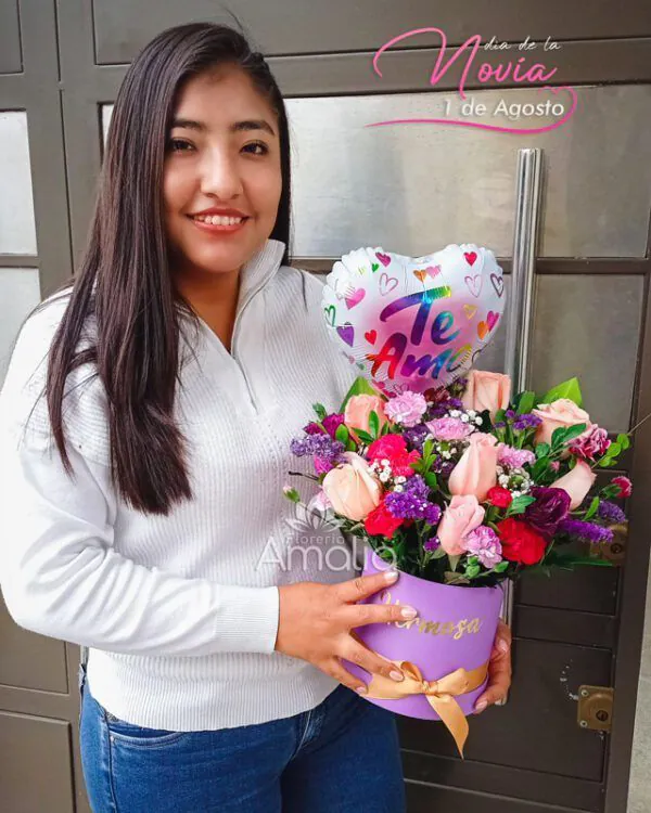 Cliente sosteniendo arreglo floral en base lila con globo corazón “Te Amo”, regalo para el Día de la Novia – Florería Amalia.