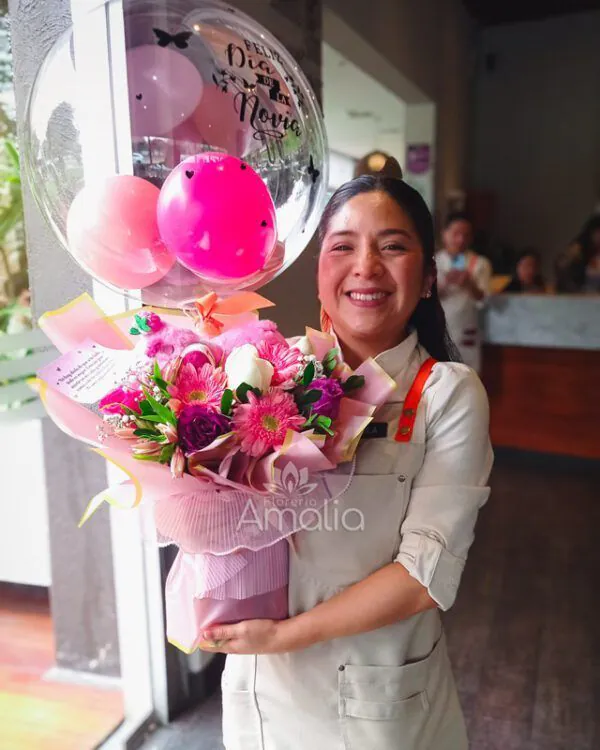 Cliente recibiendo ramo con globo burbuja “Feliz Día de la Novia”, peluche y bouquet de flores rosadas de Florería Amalia.