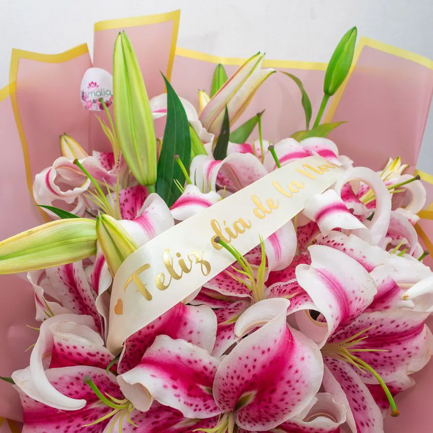 Ramo de lirios Stargazer rosados envueltos en papel rosa con cinta “Feliz Día de la Novia”.