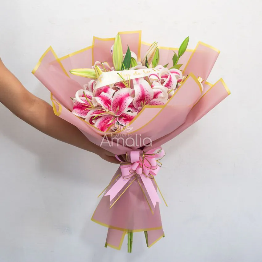 Ramo de lirios Stargazer rosados envueltos en papel rosa con cinta “Feliz Día de la Novia”.