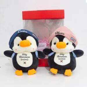 Pareja de pingüinos de peluche personalizados con nombres estampados en los gorros y fecha de aniversario en el pecho.