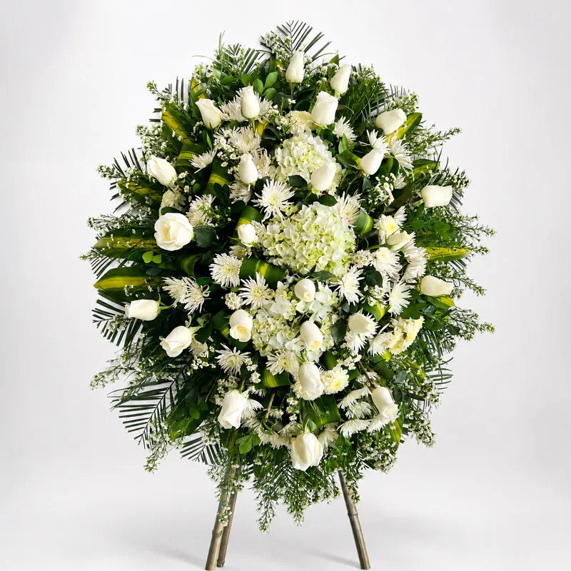 Corona fúnebre blanca con rosas, hortensias y follaje verde de Florería Amalia