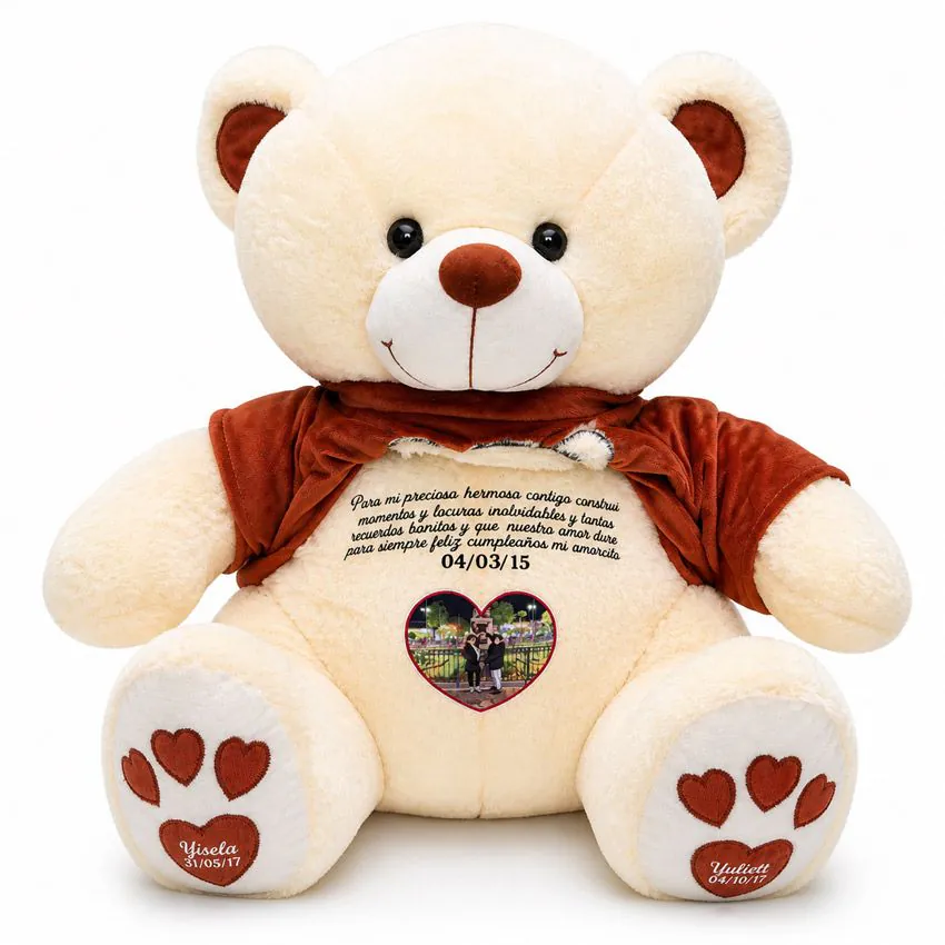 Oso de peluche beige con polera marrón levantada, mostrando un mensaje largo oculto, una foto de pareja en forma de corazón y huellas personalizadas con nombres y fechas.