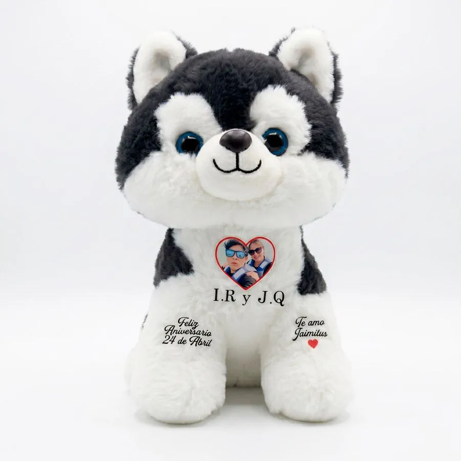 Peluche de perrito husky negro y blanco personalizado con foto en marco de corazón, iniciales y mensaje de feliz aniversario en las patitas.