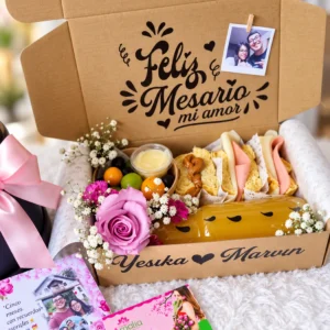 Caja con sándwiches, fruta, foto y detalle floral.