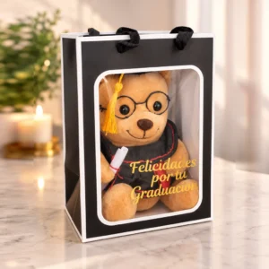 Osito con lentes, toga negra con detalles rojos, birrete y diploma. Presentado en bolsa de regalo con ventana.