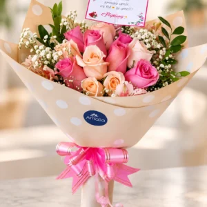 Ramo de rosas fucsias y durazno con flores blancas y lazo rosa.