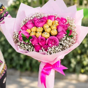 Rosas y Oro: Rosas en tonos rosa y fucsia rodean chocolates de envoltura dorada, entre pequeñas flores blancas.