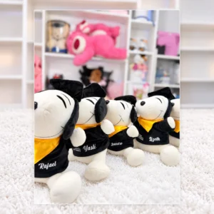 Snoopy con toga negra, birrete y pañuelo dorado. Cada uno incluye bolsa o caja de regalo.
